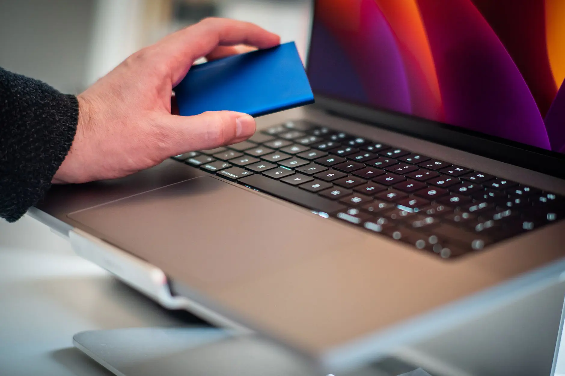 Mano sosteniendo un disco externo junto a una computadora portátil