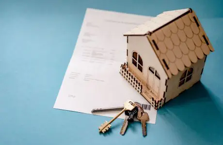 Maqueta de casa, llaves y documento sobre fondo azul
