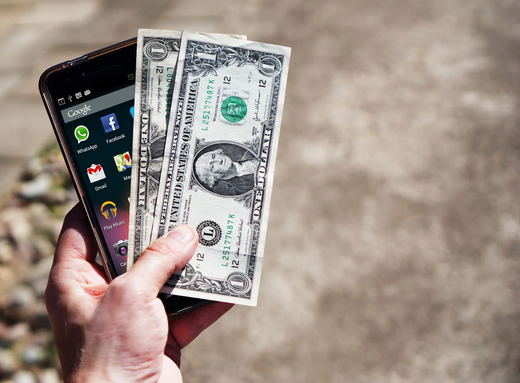 Mano con un teléfono móvil y billetes de dólares