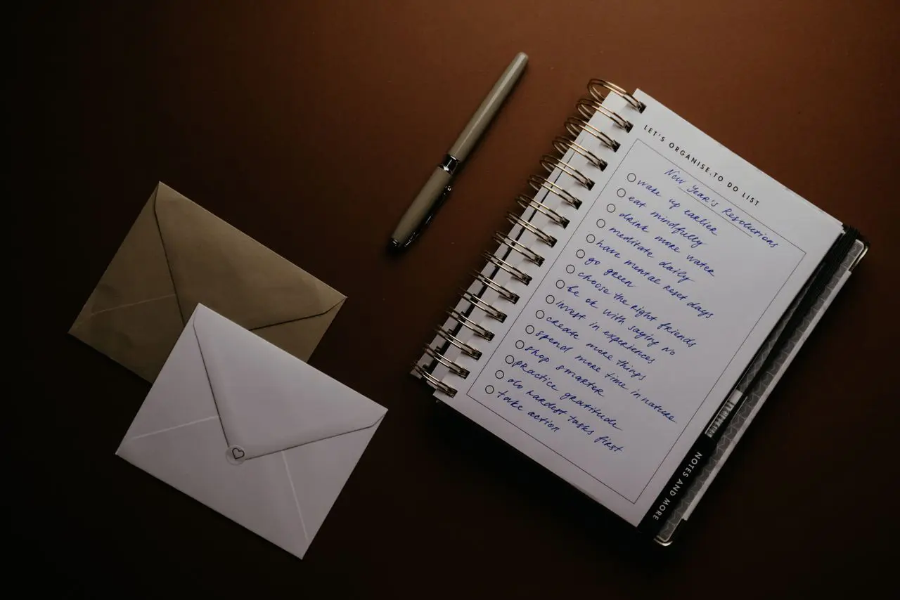 Libreta de tareas con bolígrafo y sobres sobre una mesa