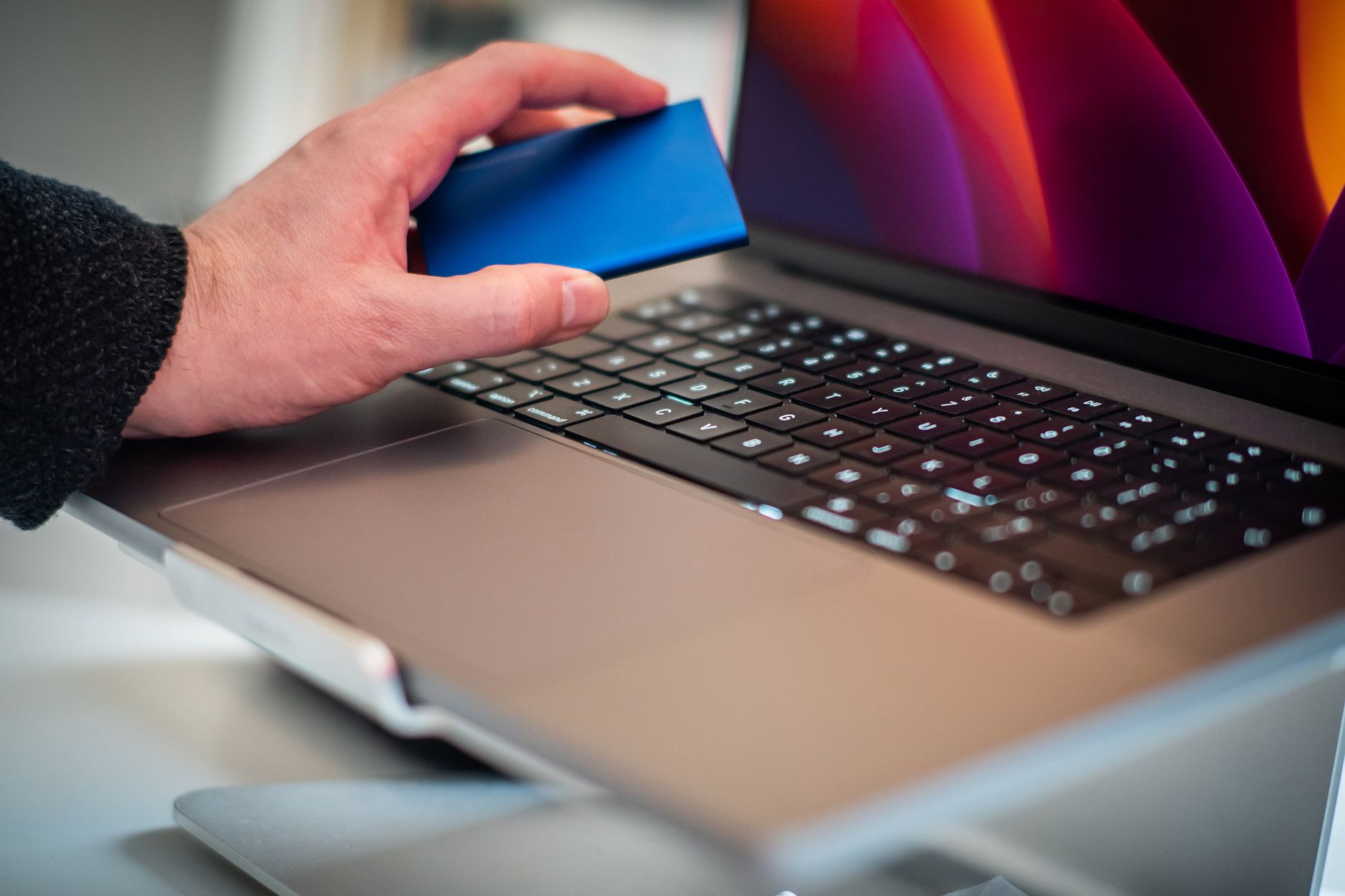 Mano sosteniendo un disco externo junto a una computadora portátil