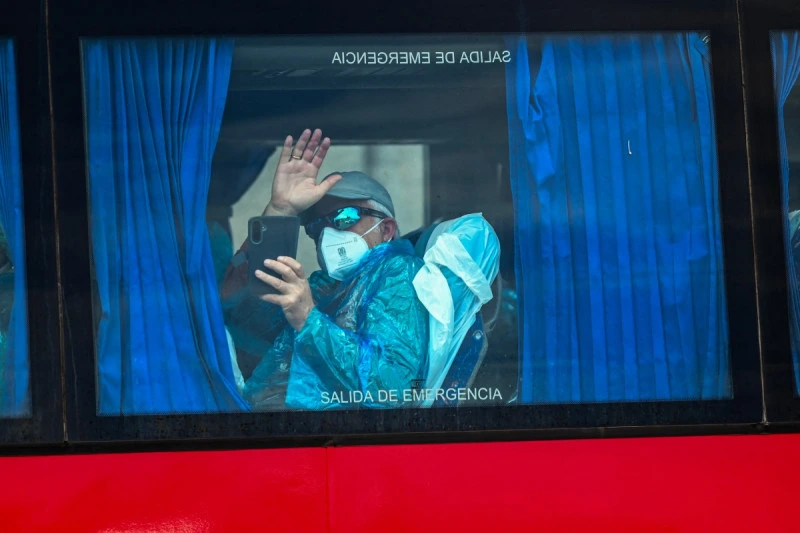 Un pasajero del crucero MV Hondius, saluda a bordo de un autobús militar tras ser trasladado en barco al puerto industrial de Granadilla de Abona, en la isla de Tenerife