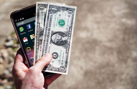 Mano con un teléfono móvil y billetes de dólares