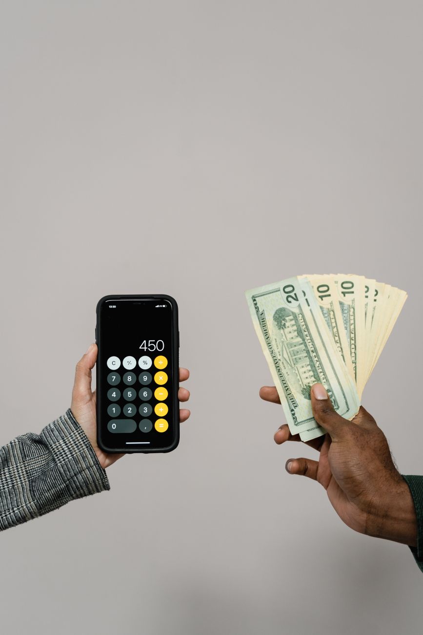 Manos con dólares y un teléfono que muestra una calculadora