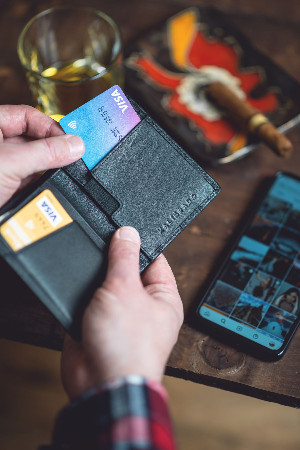 Manos sosteniendo una cartera con varias tarjetas junto a un teléfono