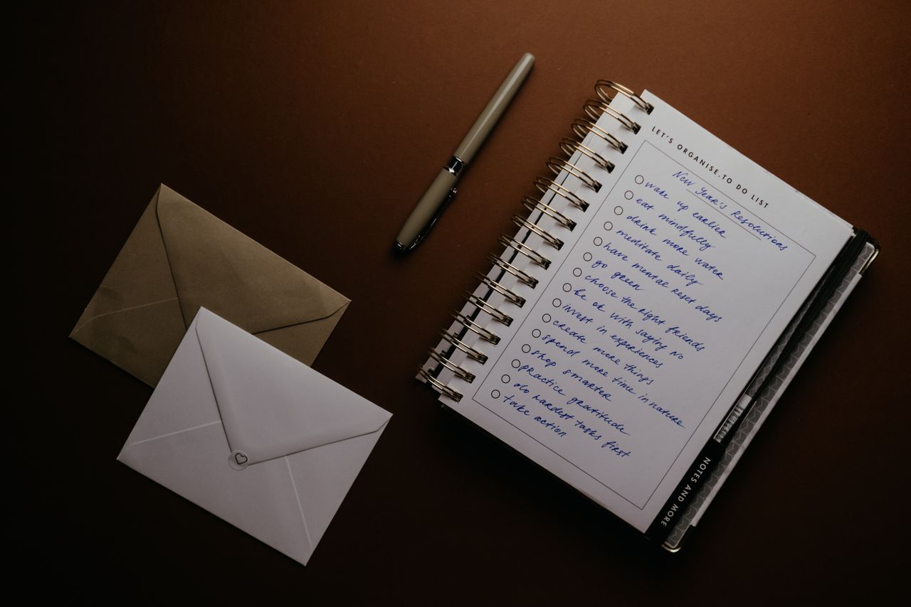 Libreta de tareas con bolígrafo y sobres sobre una mesa
