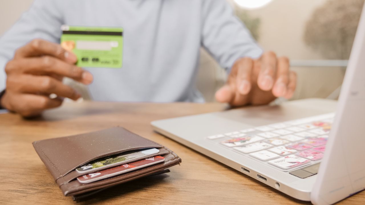 Manos sosteniendo una tarjeta bancaria junto a una computadora